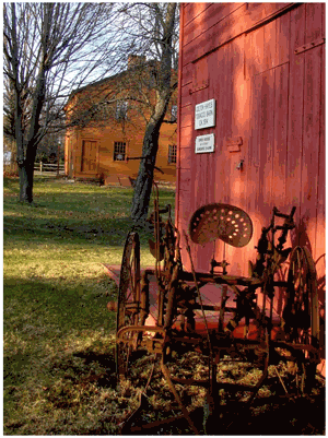 Old Farm Equipment Behind a Red Barn